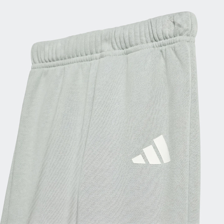 Close-up of Kids Essentials Joggers in light grey with a white Adidas logo, showing the elastic waistband and fabric.