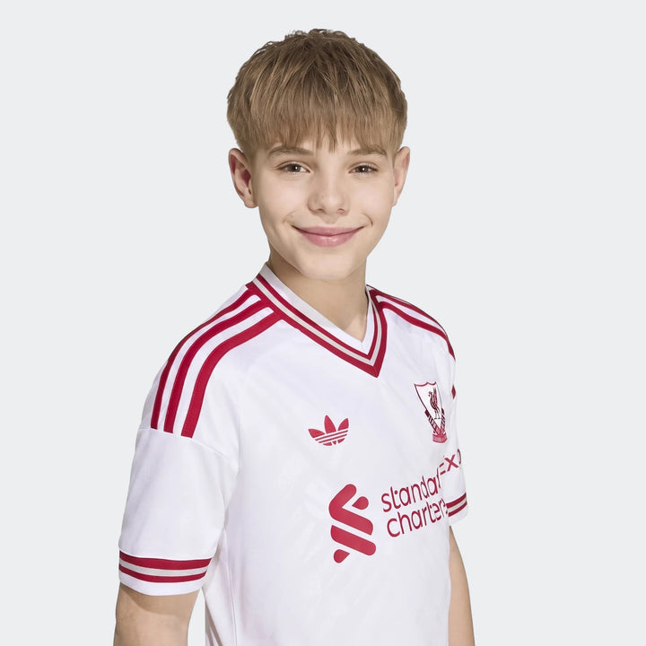 Kids Liverpool FC 26/27 Away Jersey, white with red stripes, worn by a smiling boy, presented in a studio setting.