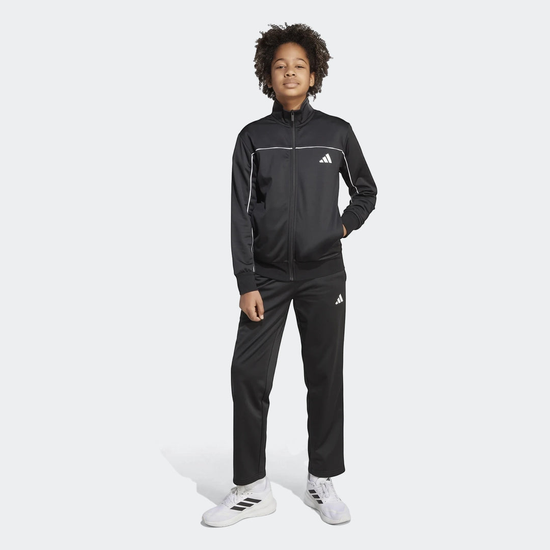 Kids Tricot Colour Pop Track Suit. Front view of a young boy wearing a black Adidas tracksuit with white details and white