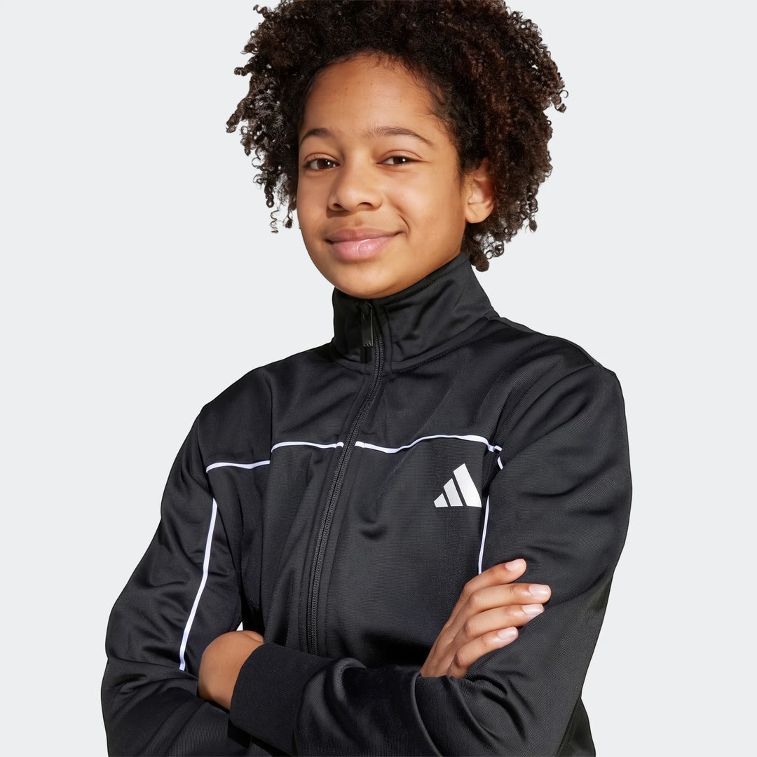 Young person wearing a black Kids Tricot Colour Pop Track Suit with white stripes and Adidas logo. Half-body shot of the