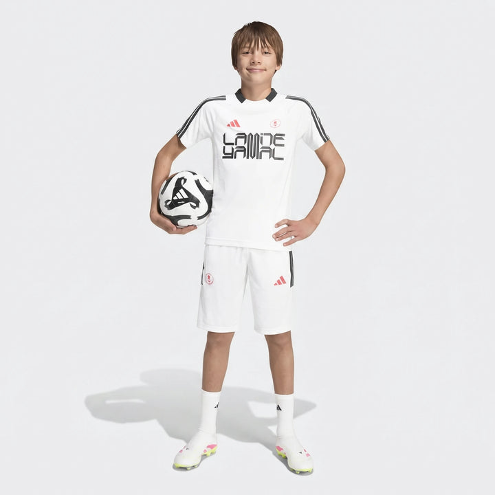 White Lamine Yamal training t-shirt for kids, worn by a boy in a full-body shot, paired with matching shorts and holding a