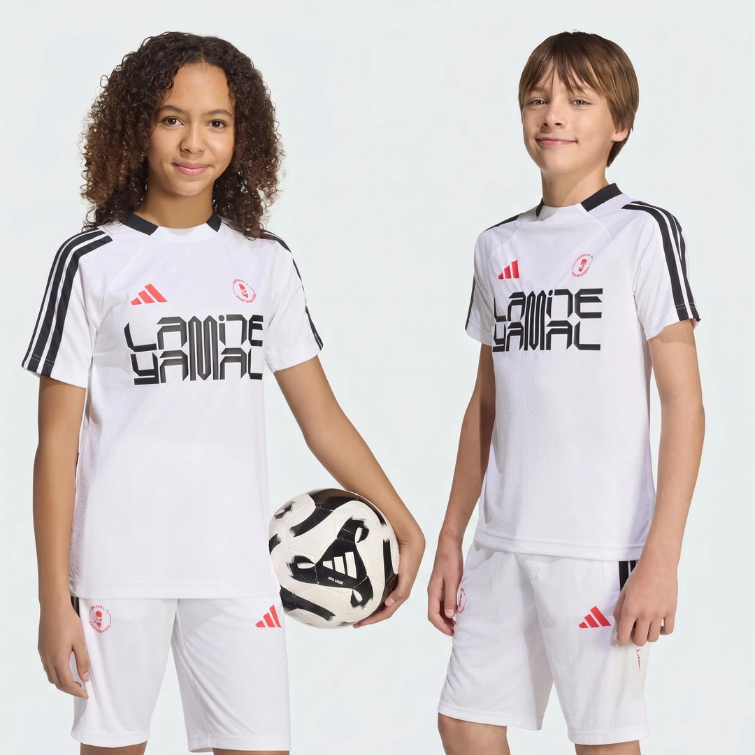 Two children model a white Lamine Yamal training t-shirt and shorts set, with one holding a black and white soccer ball.
