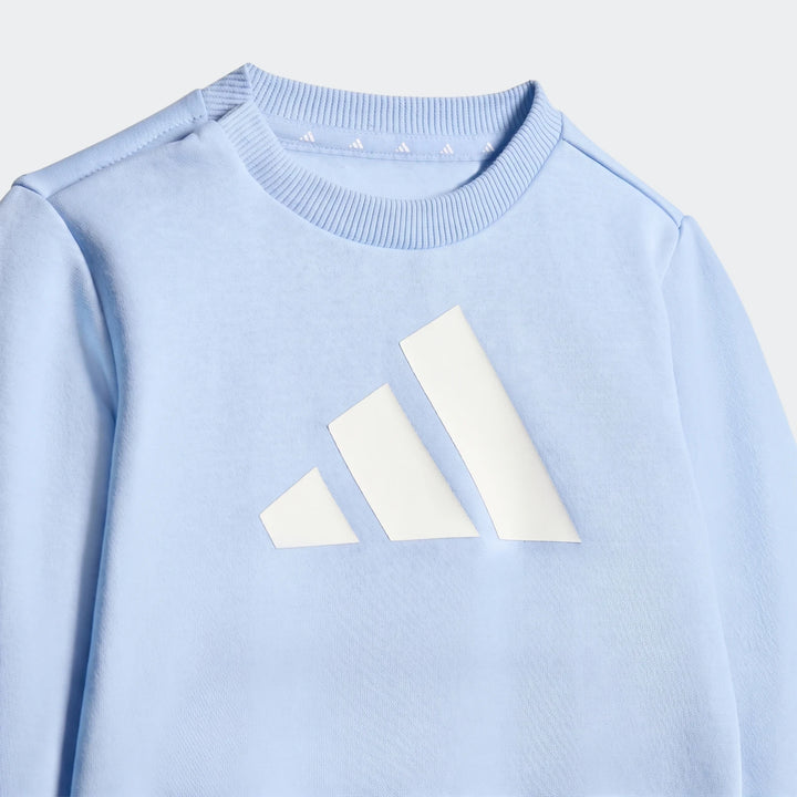 Close-up of a light blue Adidas Essentials Jogger Set sweatshirt featuring a prominent white Adidas Badge of Sport logo on