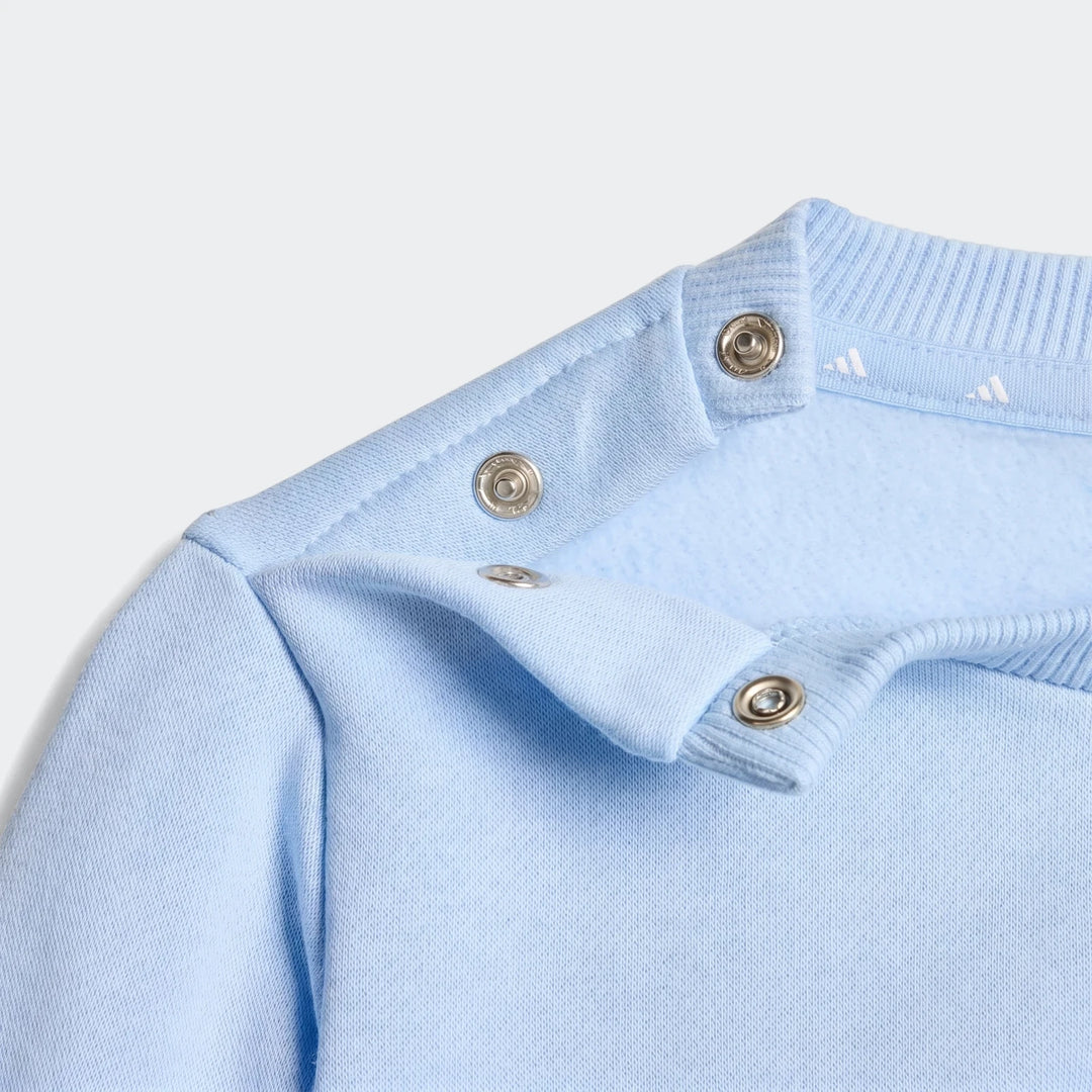 Close-up of a light blue Adidas Kids Essentials sweatshirt shoulder with snap buttons and ribbed neckband.