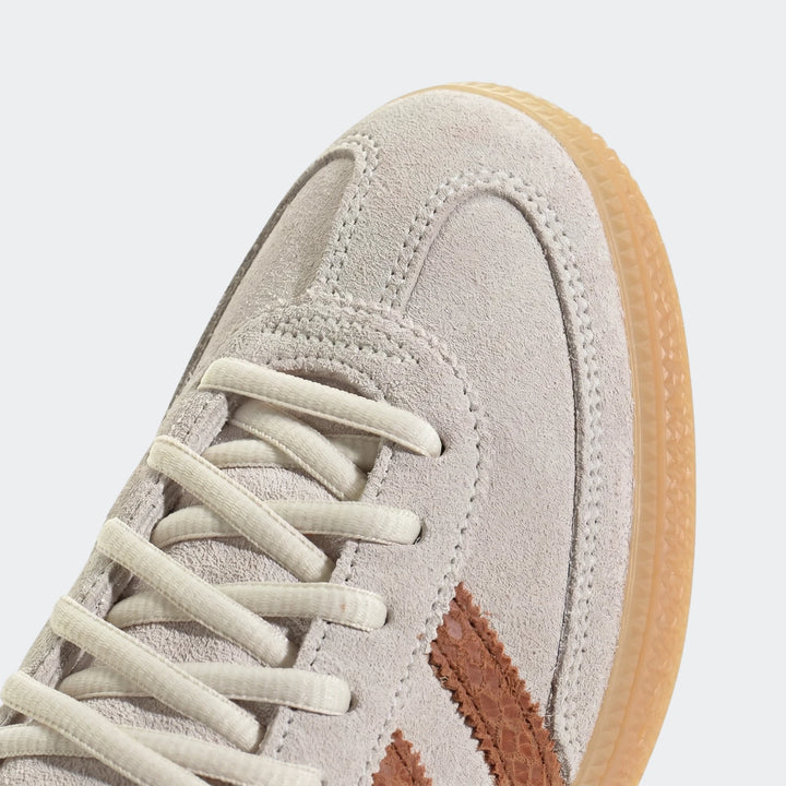 Close-up of a light grey suede sneaker with brown stripes and cream laces, showing the toe box and lacing.