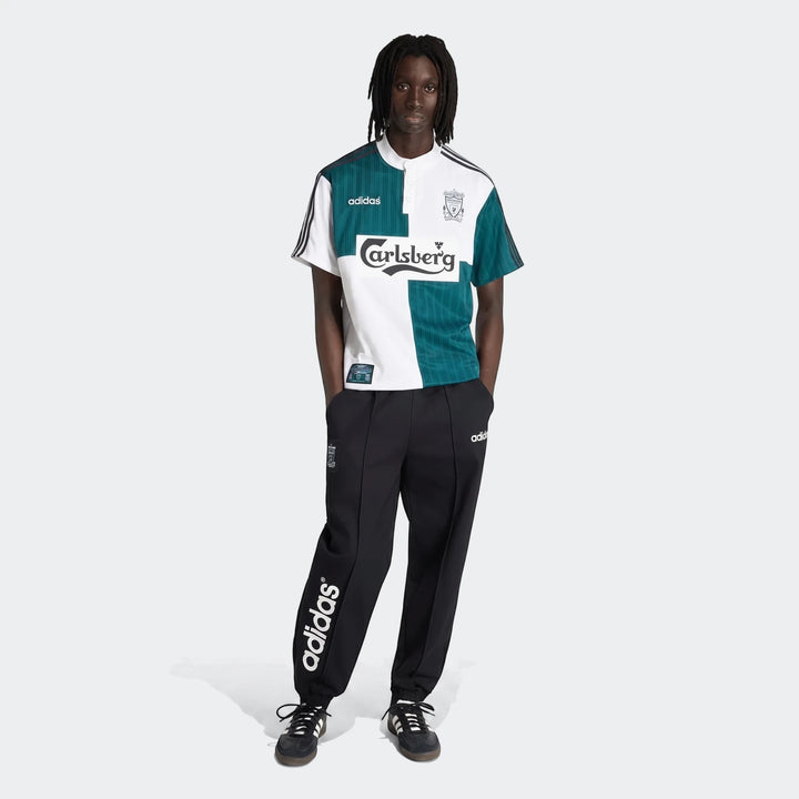 Male model wearing a green and white Liverpool Fc 1995 Away Jersey and black Adidas track pants and sneakers, full body view.