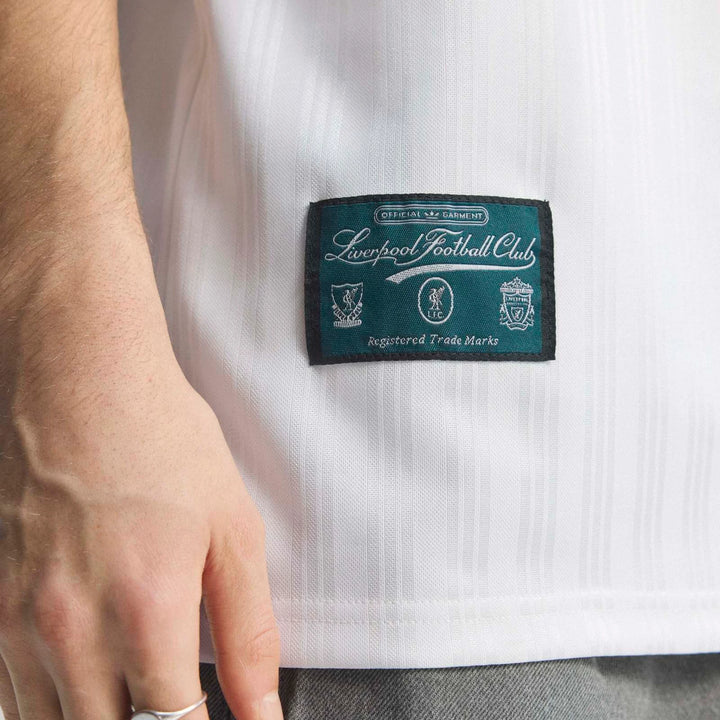 Close-up of a person wearing a white Liverpool Fc 1995 Away Jersey, highlighting the detailed "Liverpool Football Club"