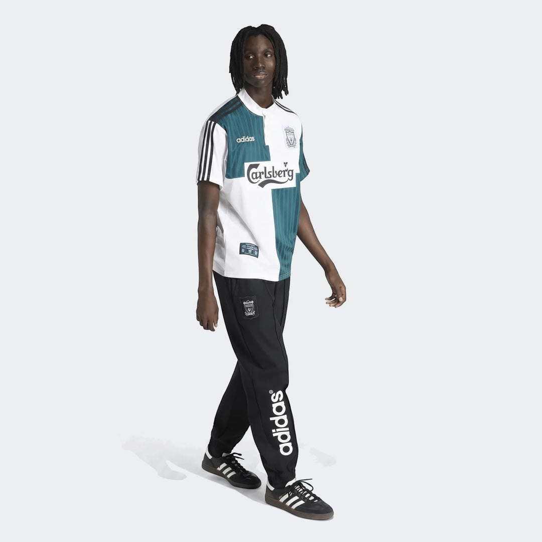 Male model wearing a vintage white and teal Liverpool FC 1995 away jersey, black Adidas track pants, and black sneakers.