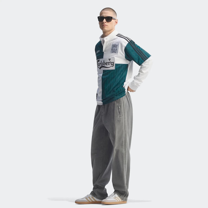 Male model wearing a vintage Liverpool FC 1995 Away Jersey in white and teal, paired with gray sweatpants and white sneakers.