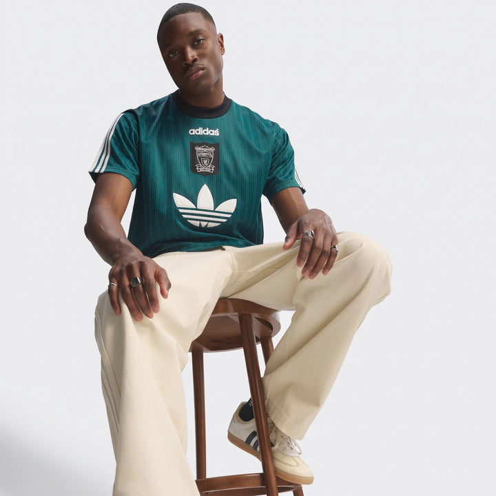 Young man modeling a green Adidas Liverpool FC 1995 Poly T-shirt, paired with cream trousers and white sneakers.