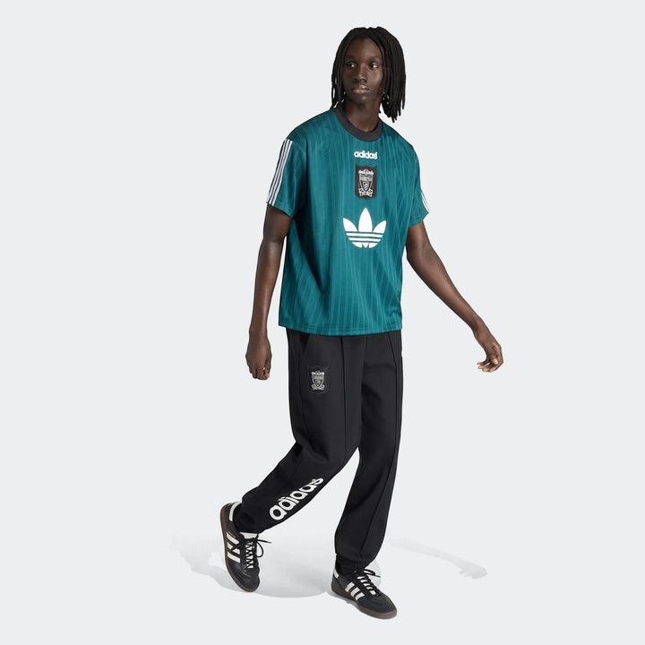 Male model wearing a teal Adidas Liverpool FC 1995 Poly T-Shirt, black track pants, and black Adidas sneakers.