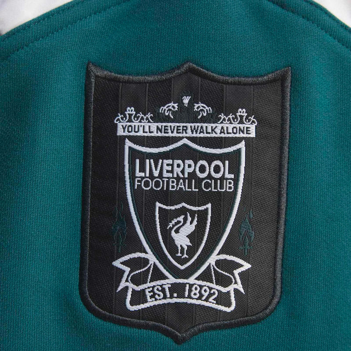 Close-up of a green Liverpool FC 1995 sweatshirt showing the embroidered crest with 'YOU'LL NEVER WALK ALONE'.
