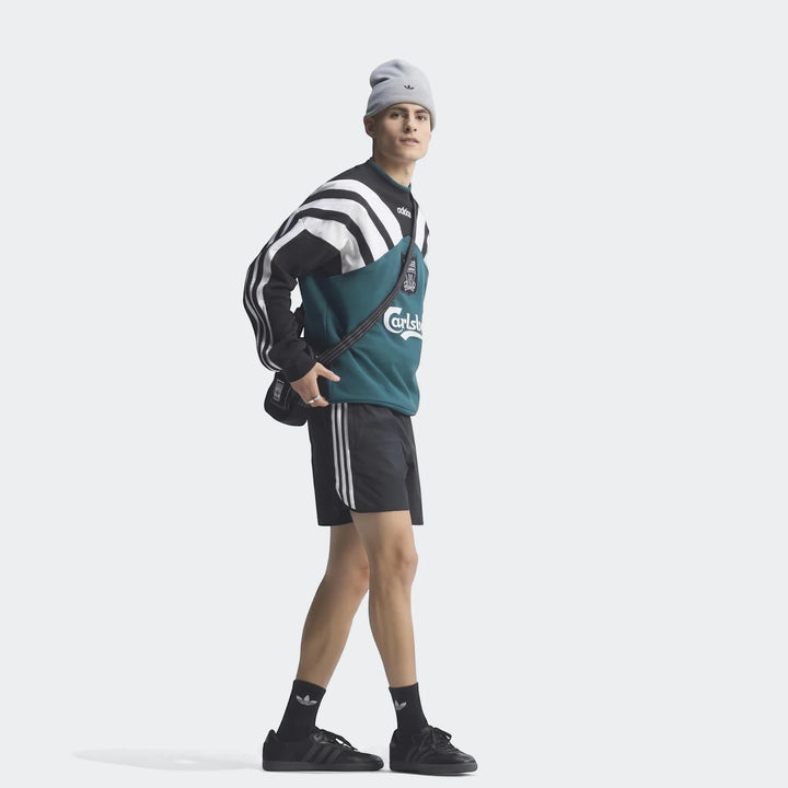 Male model wearing a vintage black, white, and teal Liverpool FC 1995 sweatshirt, black striped shorts, and black sneakers.