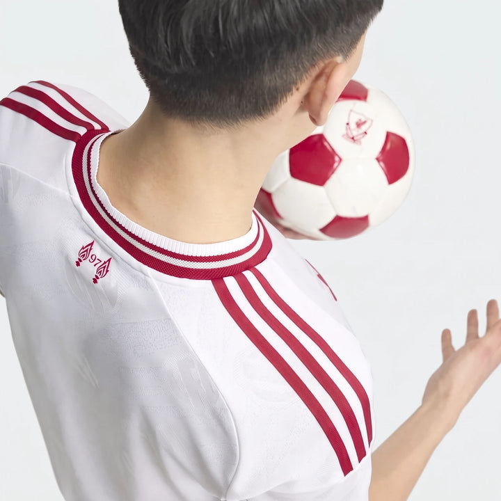 Rear view of a person wearing a white and red Liverpool FC 26/27 Away Authentic Jersey, heading a white and red soccer ball.