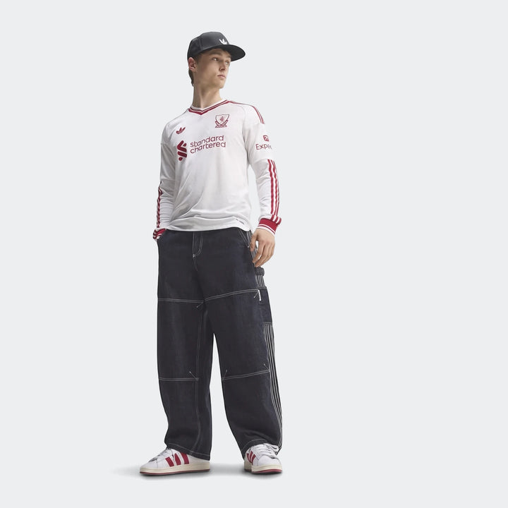 Male model wearing a white Liverpool FC 26/27 Away Authentic Longsleeve Jersey, dark blue baggy jeans, and white sneakers.