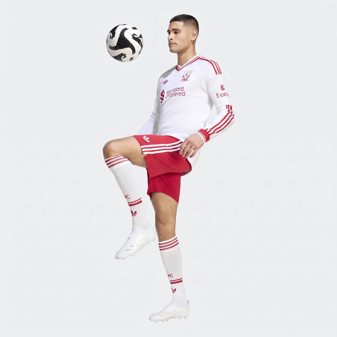 Male model wearing a white Liverpool FC 26/27 Away Authentic Longsleeve Jersey with red accents, red shorts, and white