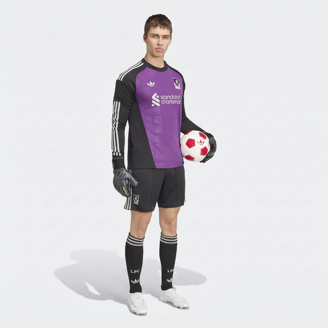 Full body shot of a male model wearing the Liverpool FC 26/27 Away Goalkeeper Jersey in purple and black, holding a soccer