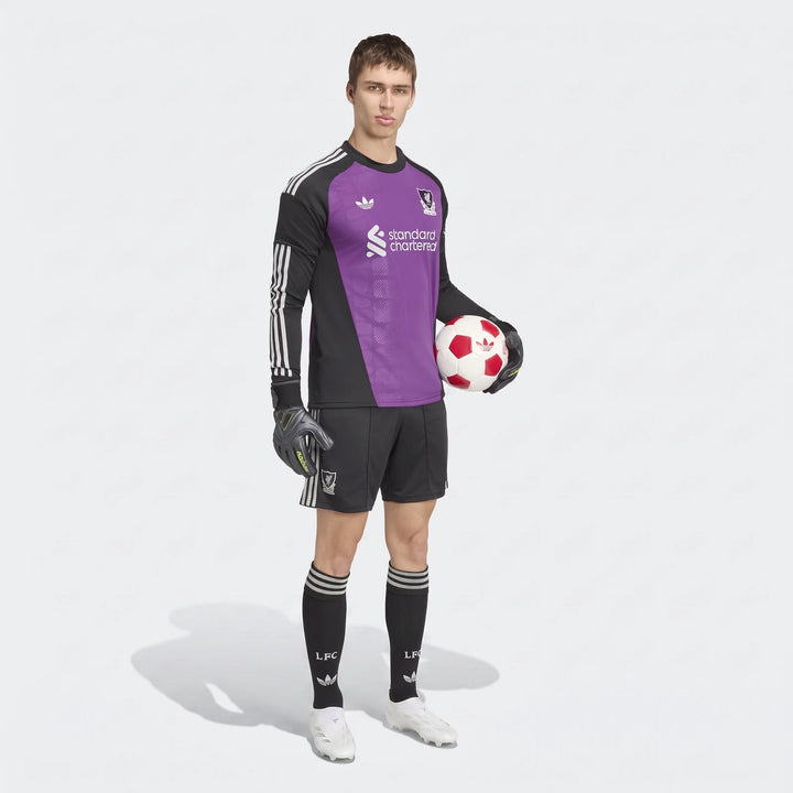 Full body shot of a male model wearing the Liverpool FC 26/27 Away Goalkeeper Jersey in purple and black, holding a soccer