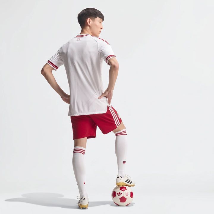 Male model in an authentic Liverpool FC 26/27 away jersey, white with red trim, red shorts, and white socks, with his foot