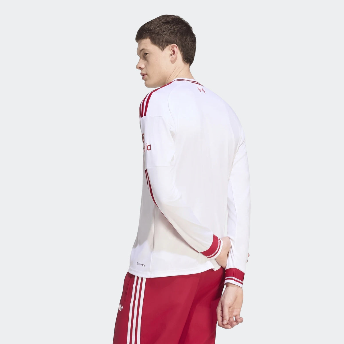 Male model wearing a white Liverpool FC 26/27 away long-sleeve jersey with red stripes and matching red shorts, viewed from