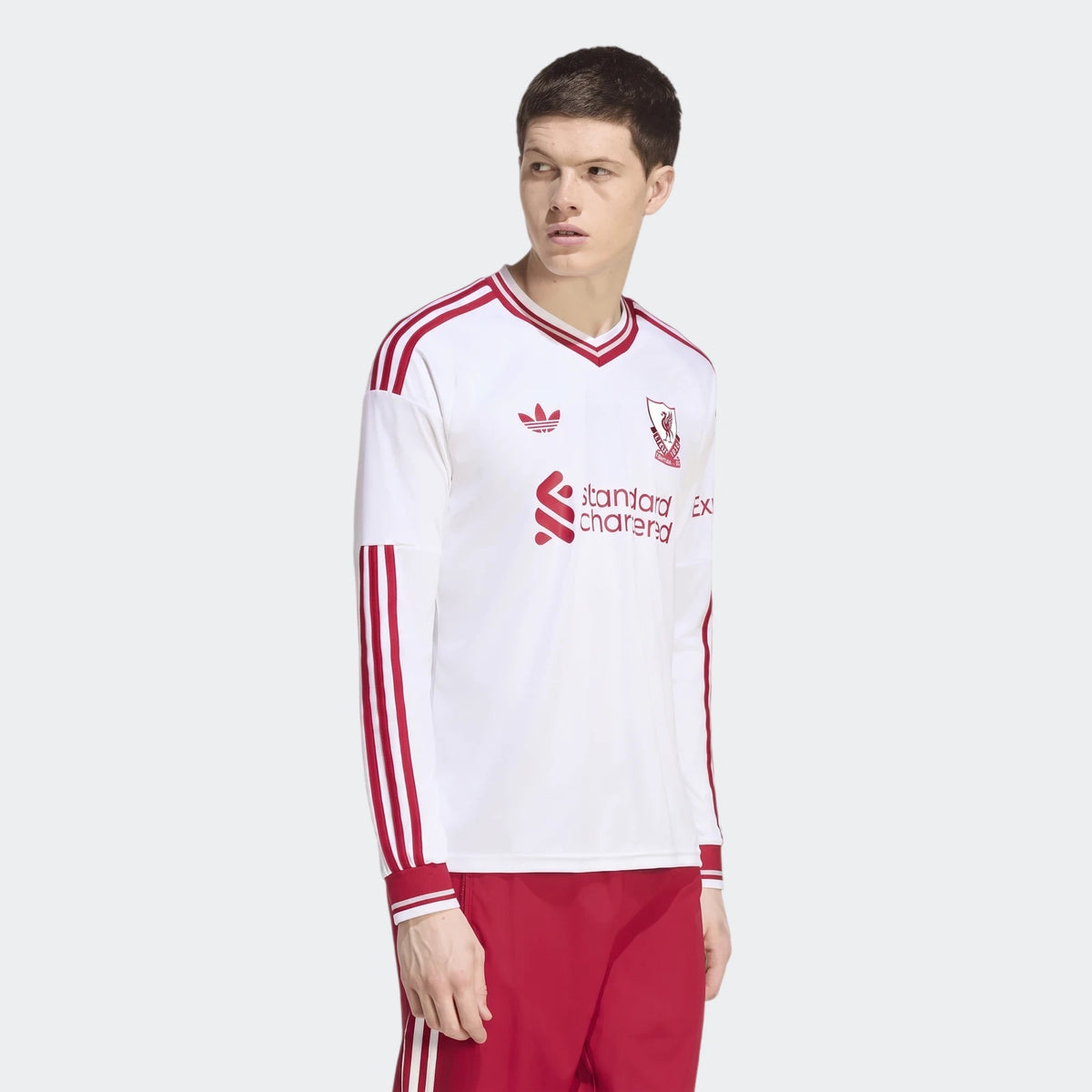 Male model wearing a white Liverpool FC 26/27 away long sleeve jersey with red stripes on the shoulders and sleeves, and red