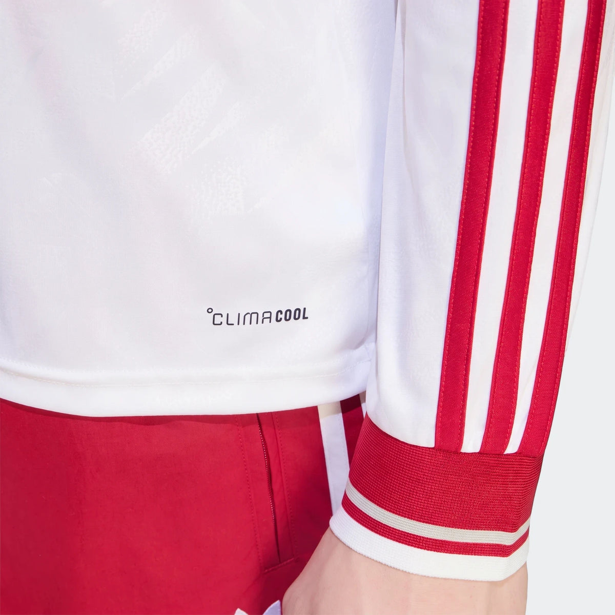 Close-up of a white Liverpool FC 26/27 Away Longsleeve Jersey with red shoulder stripes and a ribbed cuff on a person.