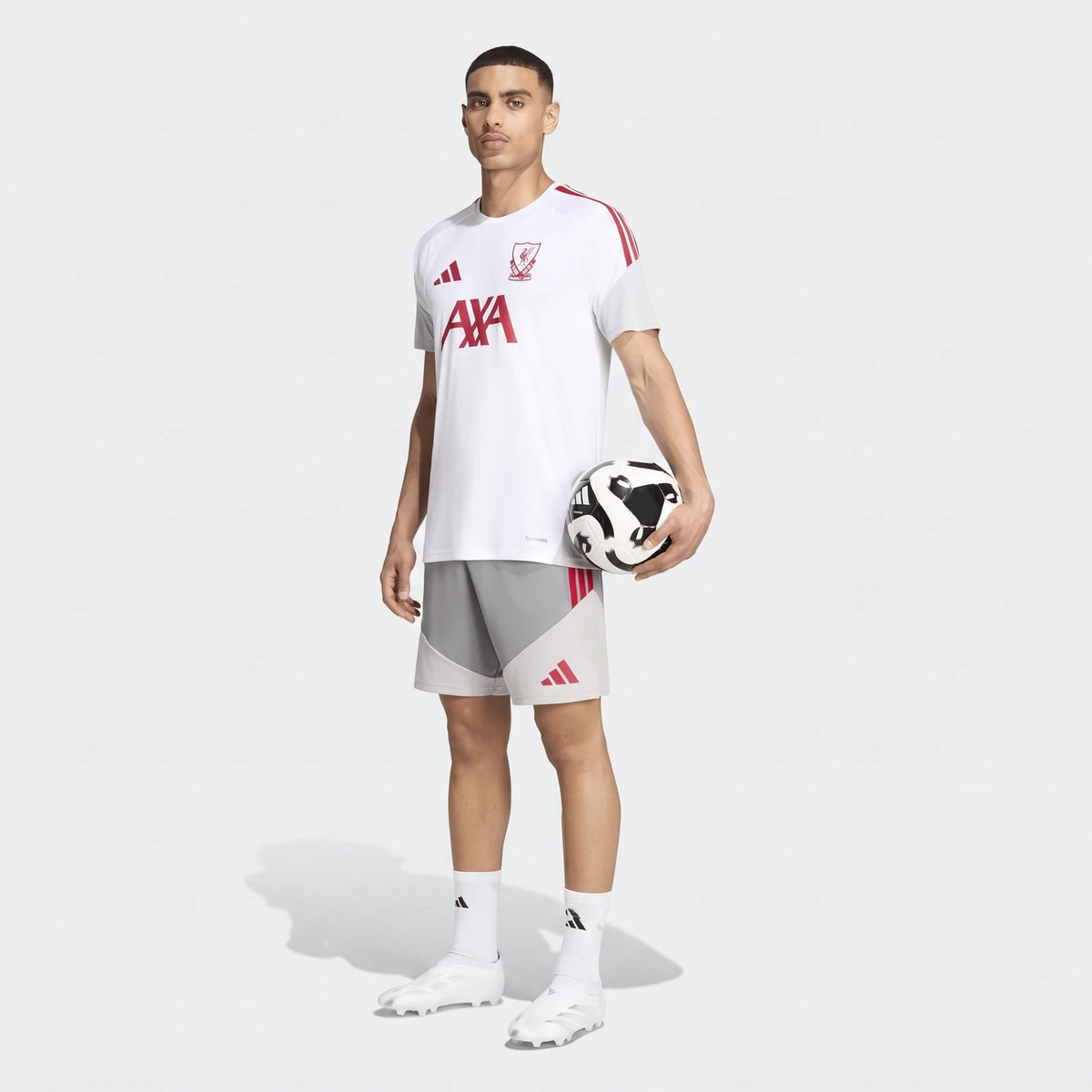 Male model wearing a white Liverpool FC 26/27 Cup Tiro Training Jersey with red accents and grey shorts, holding a football.