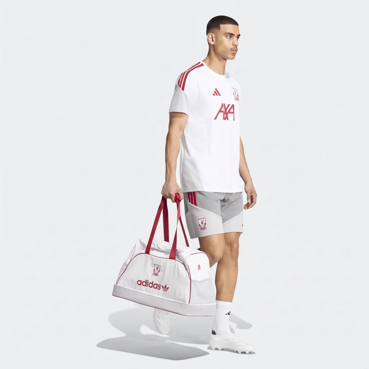 Male model in a white and red Liverpool FC 26/27 Cup Tiro training jersey and grey shorts, carrying a white Adidas duffel