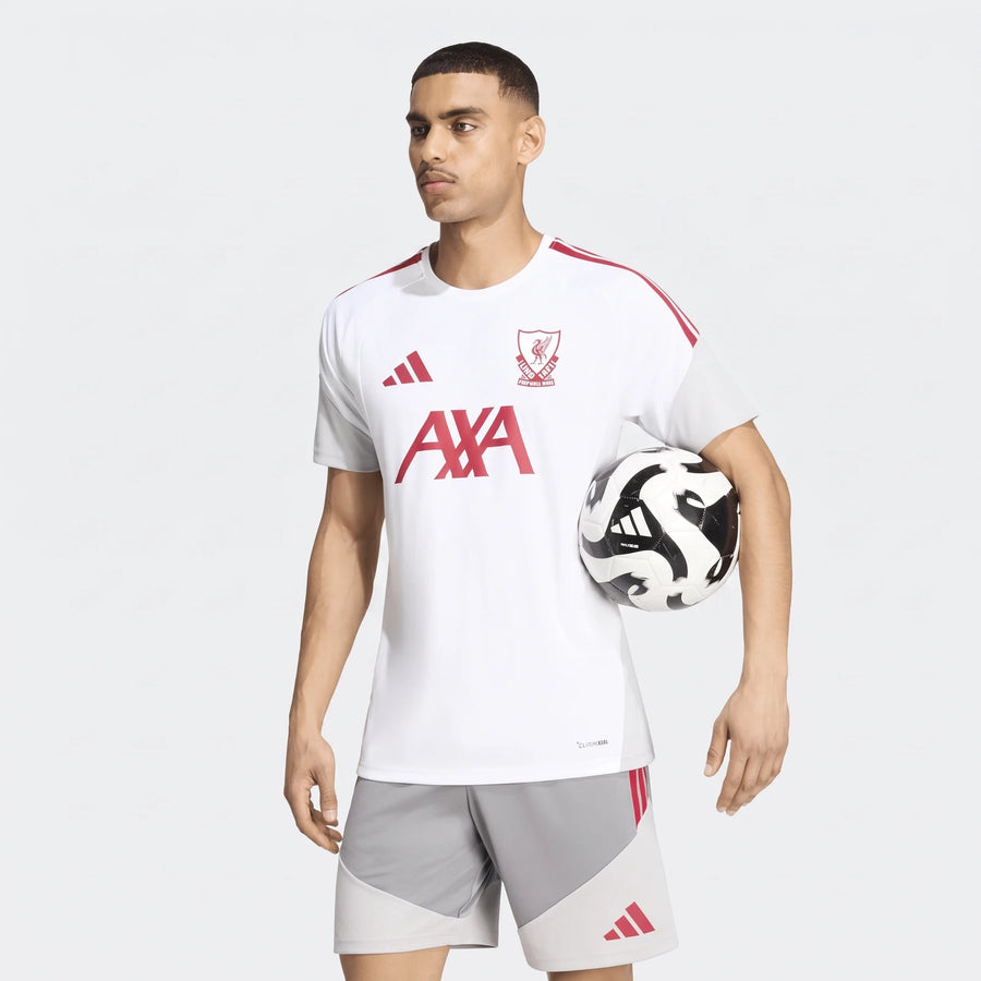 Male model wearing a white Liverpool FC 26/27 Cup Tiro Training Jersey with red accents and grey shorts, holding a black and