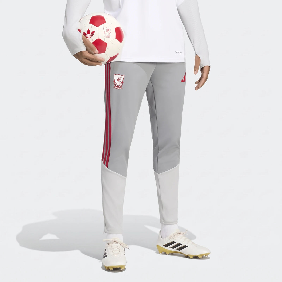 Gray Liverpool FC 26/27 Cup Tiro Training Pants with red stripes and club crest, worn by a person holding a soccer ball.