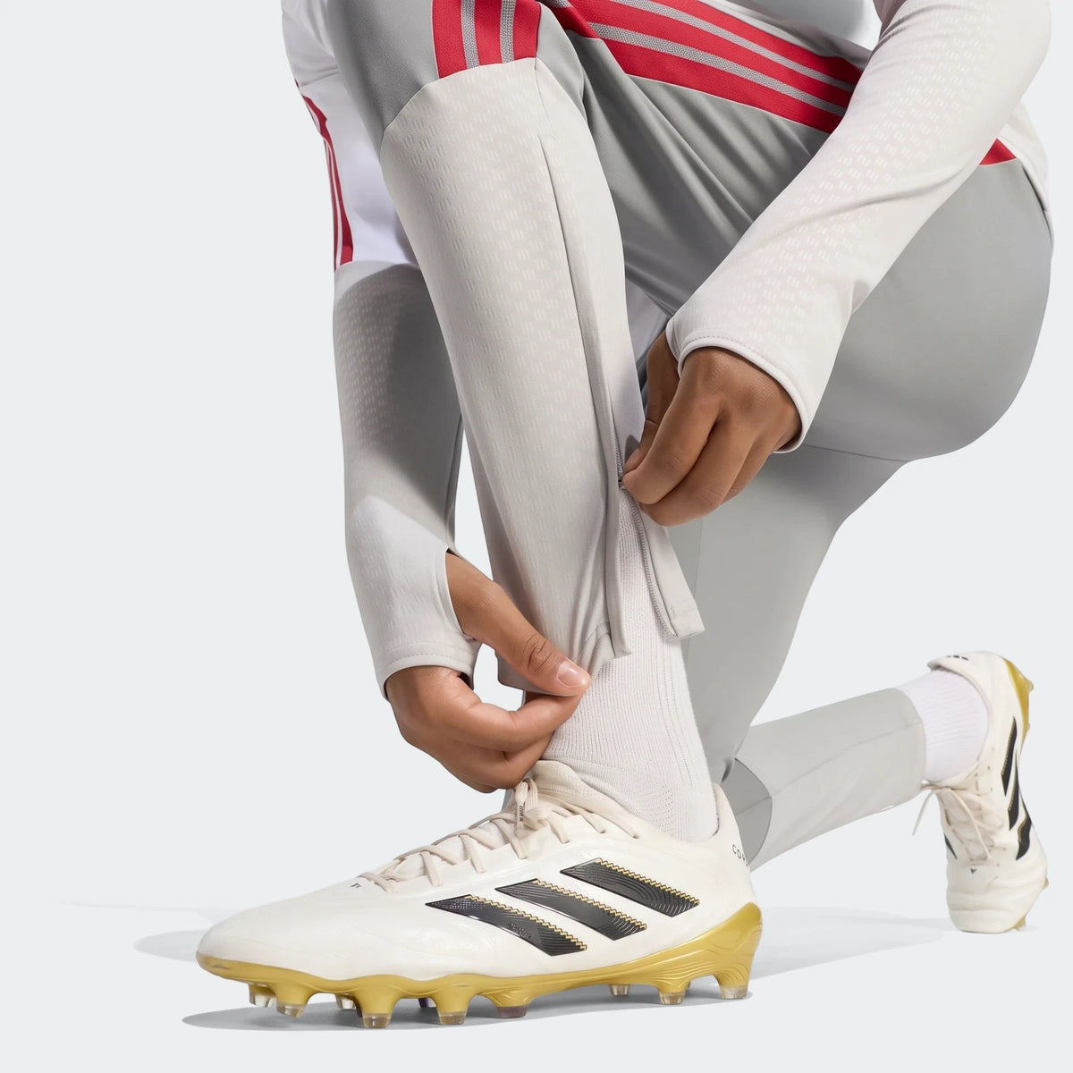 Close-up of gray Liverpool FC 26/27 Cup Tiro training pants with red stripes and ankle zippers, worn by a person.