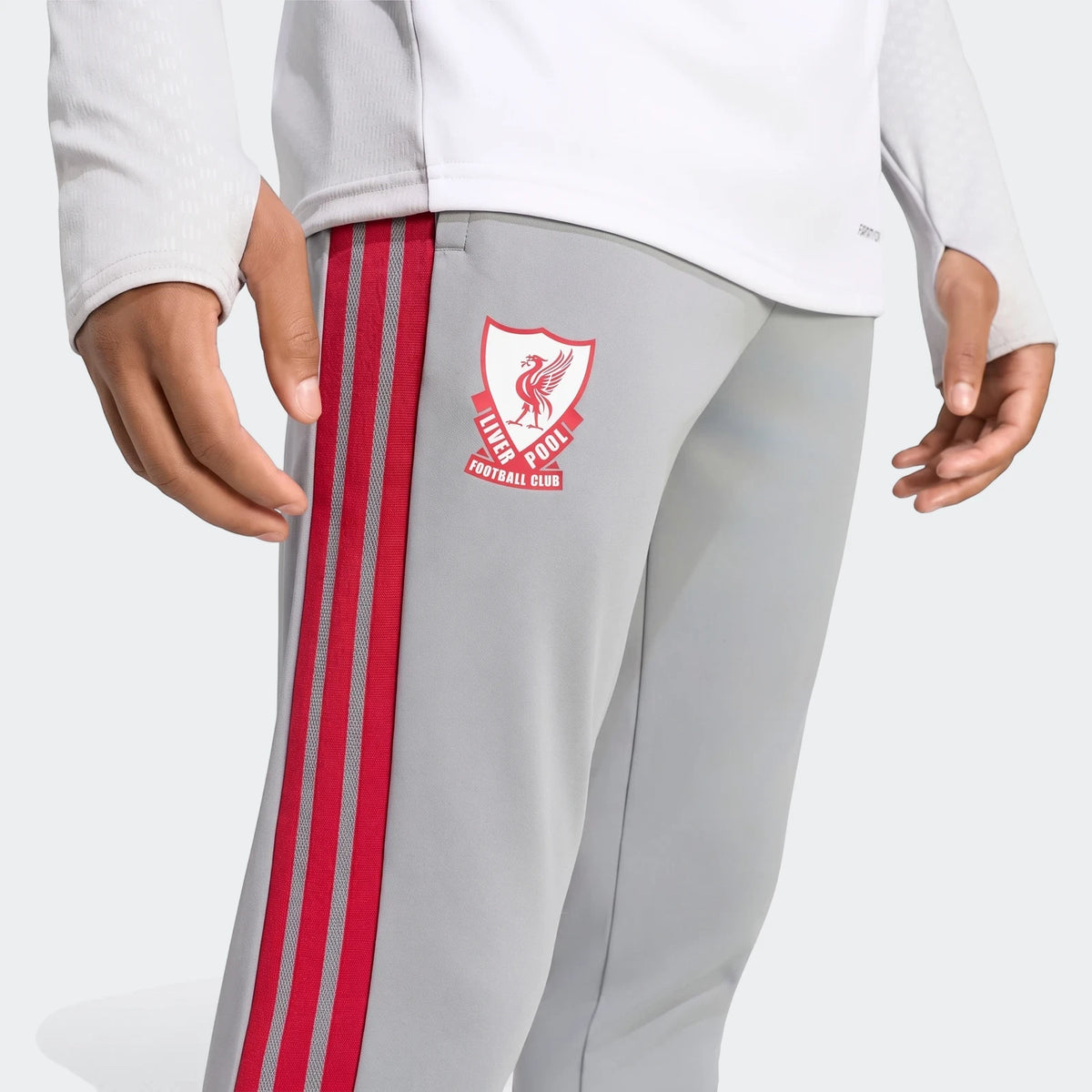 Close-up of a person wearing grey Liverpool FC 26/27 Cup Tiro training pants with red side stripes and a white long-sleeved