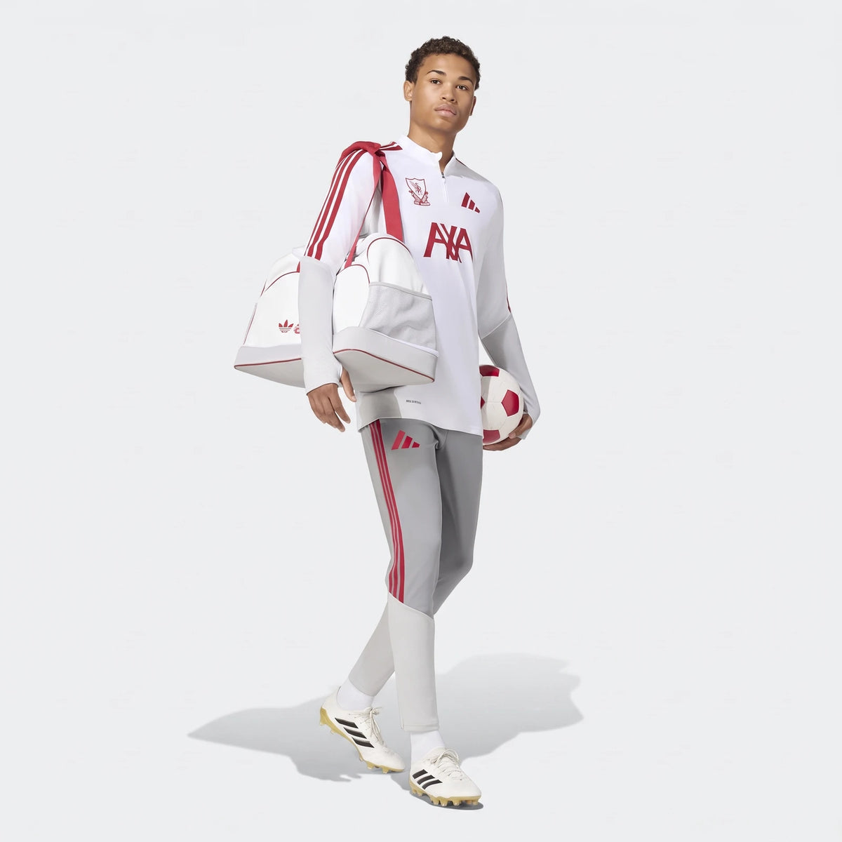 Young man wearing Liverpool FC 26/27 Cup Tiro Training Pants, a white training top, and carrying a duffel bag and soccer