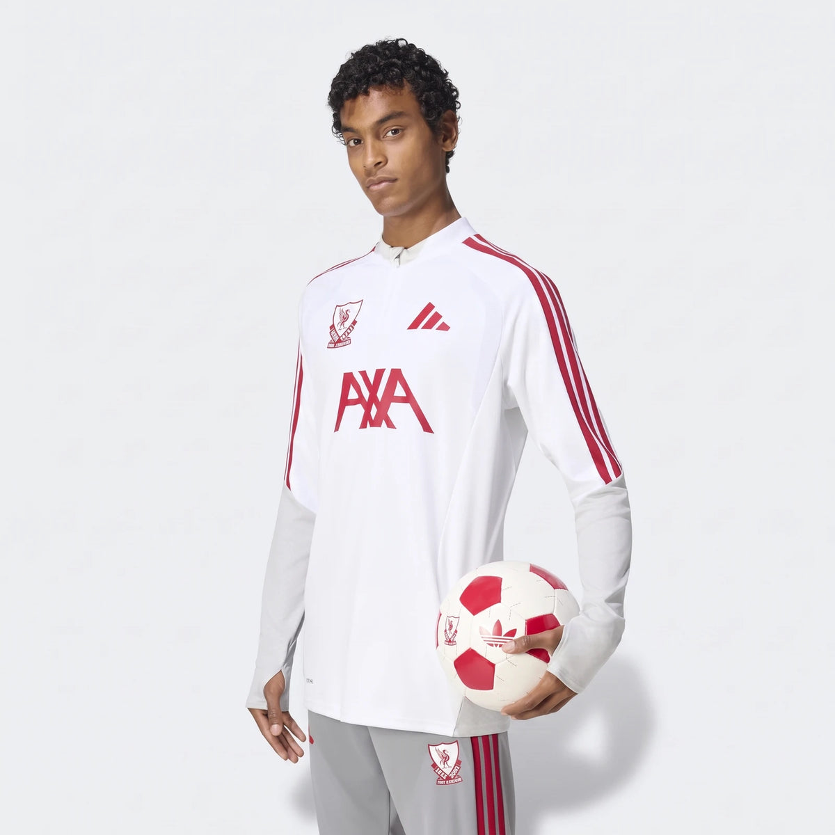 A young man wearing the white and grey Liverpool FC 26/27 Cup Tiro Training Top, holding a red and white soccer ball.
