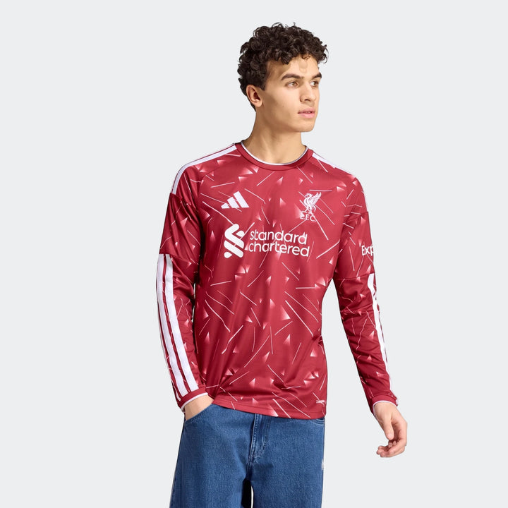 Male model wearing a red Liverpool FC 26/27 home long-sleeve jersey with white patterns, sponsor logos, and blue jeans.