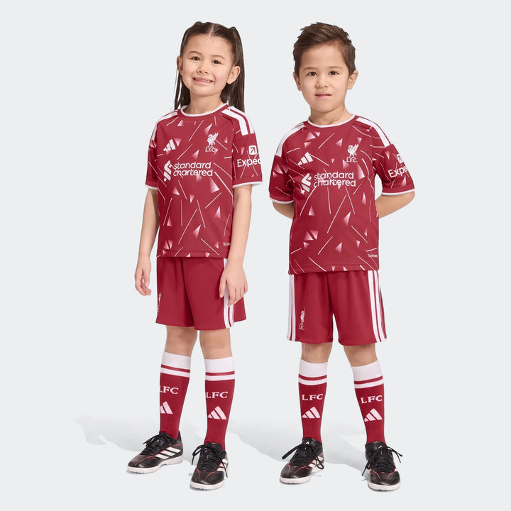 Two young children wearing the Liverpool FC 26/27 Home Kids Set, featuring a burgundy and white patterned jersey, shorts,