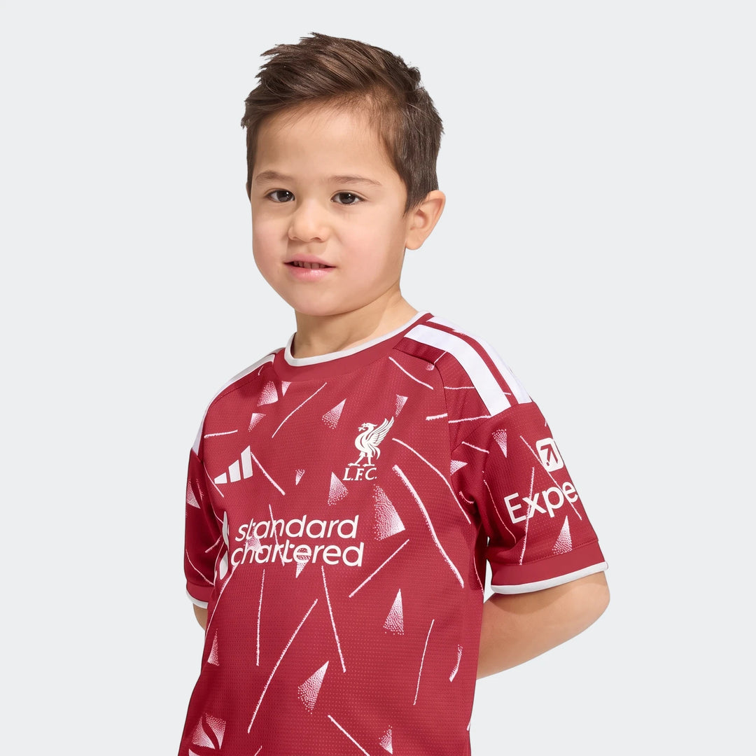 Young boy wearing a red Liverpool FC 26/27 Home Kids Set jersey with white patterns and sponsor logos.