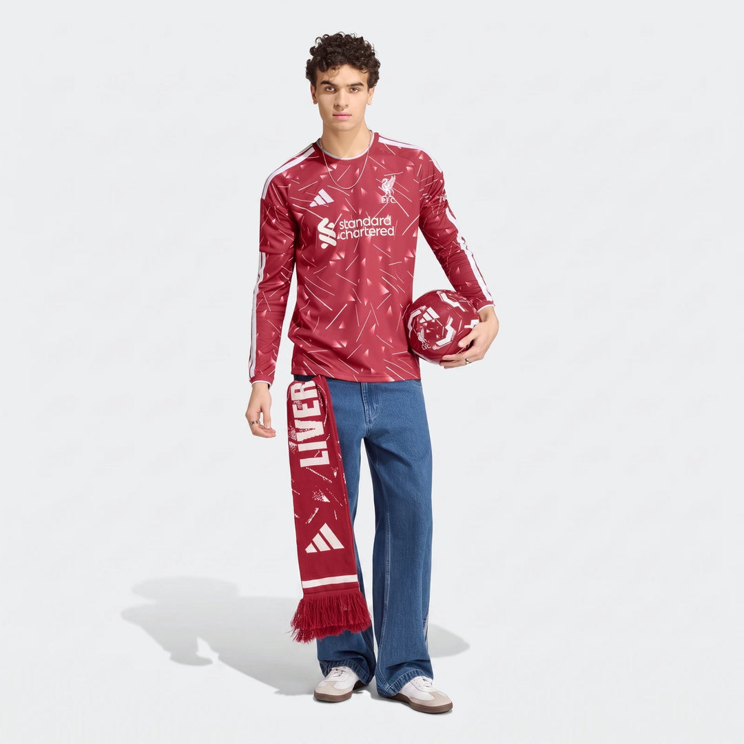 Male model wearing a red Liverpool FC 26/27 home long sleeve jersey with white patterns, holding a matching football and