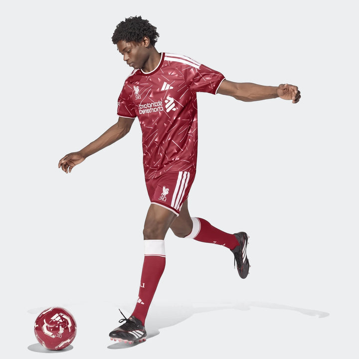 Male model wearing red and white Liverpool FC 26/27 home shorts and jersey, captured mid-kick with a matching soccer ball.