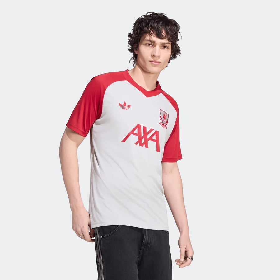 Male model wearing a white and red Adidas Liverpool FC 26/27 pre-match jersey and dark jeans.