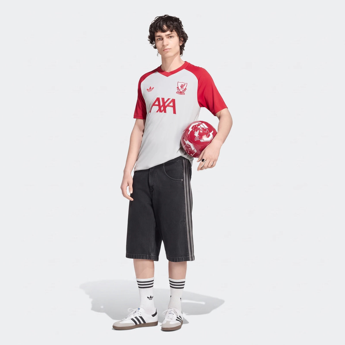 A male model showcases the red and white Liverpool FC 26/27 Pre Match Jersey, paired with black shorts and holding a