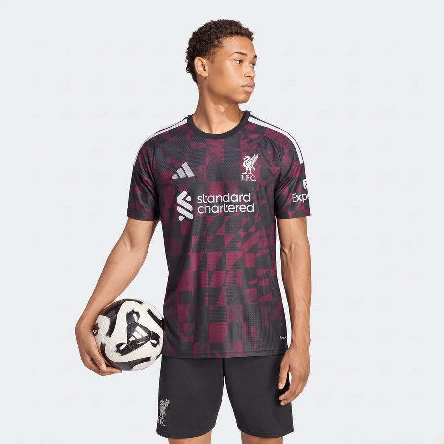 Male model wearing a Liverpool FC 26/27 Third Authentic Jersey in black and maroon geometric pattern, holding a soccer ball.