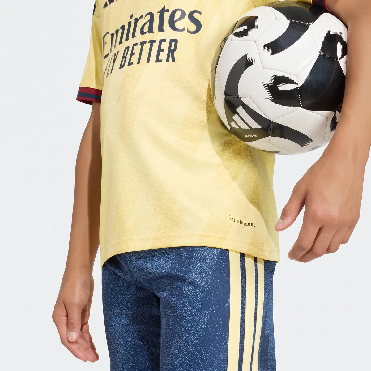 Close-up of a person wearing a yellow Liverpool FC 26/27 Third Jersey and blue shorts, holding a black and white soccer ball.