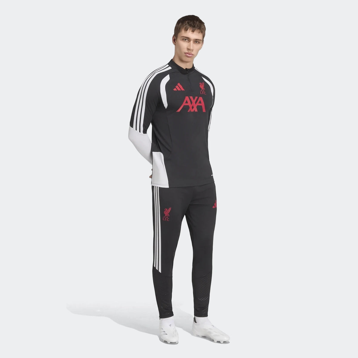 Male model in black Liverpool FC 26/27 Tiro training tracksuit with white Adidas stripes and red logos, white soccer cleats.