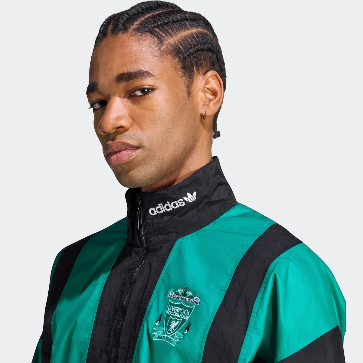 Close-up of a man wearing a black and green Adidas Liverpool FC EQT Track Top with a club crest and braided hair.