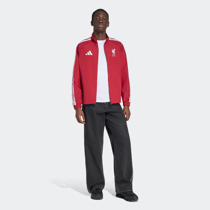 Liverpool Fc Home Anthem Jacket in red with white stripes and team logos, worn by a male model over a white tee and dark