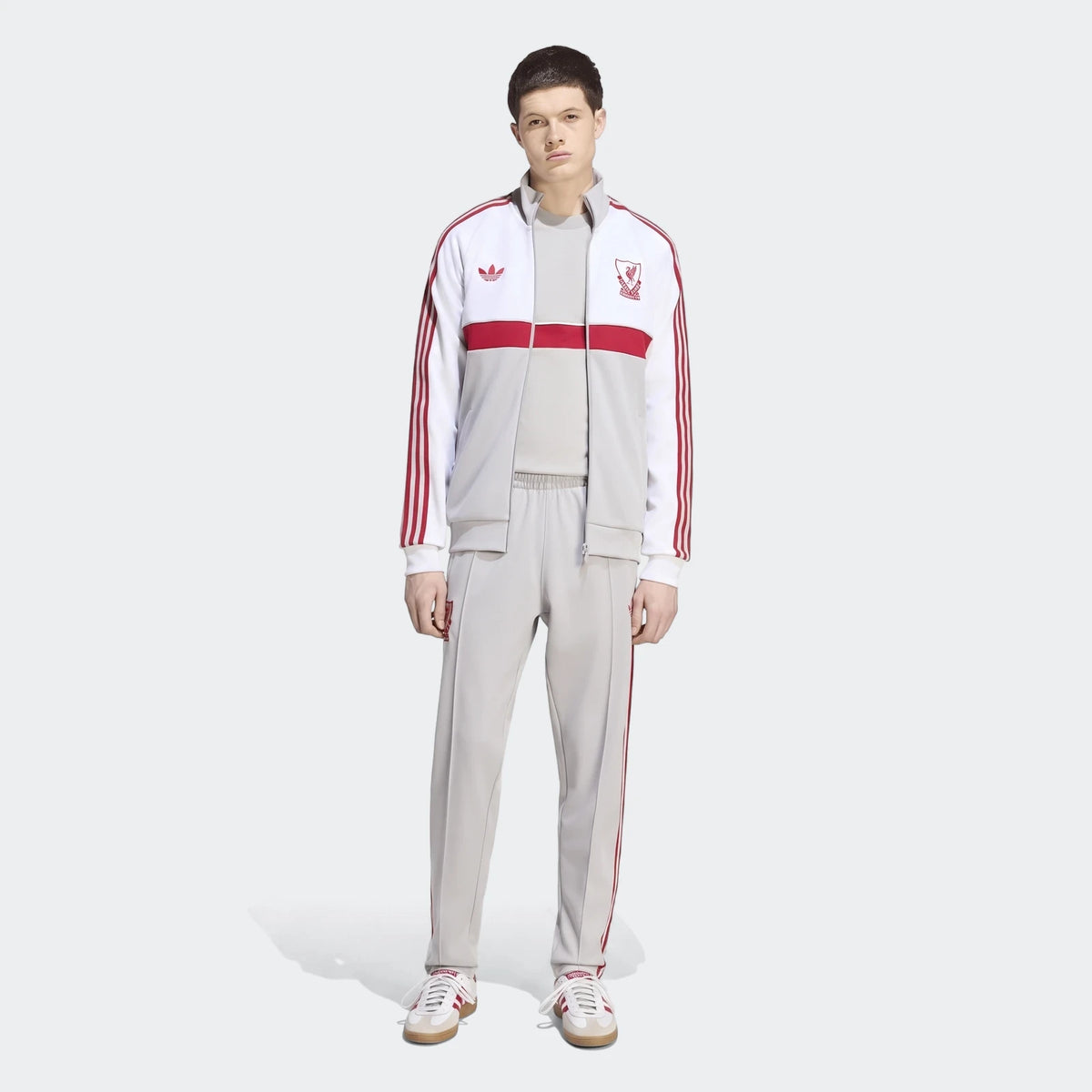 Male model wearing a full Liverpool FC Originals grey and red tracksuit with white Adidas stripes and white sneakers,
