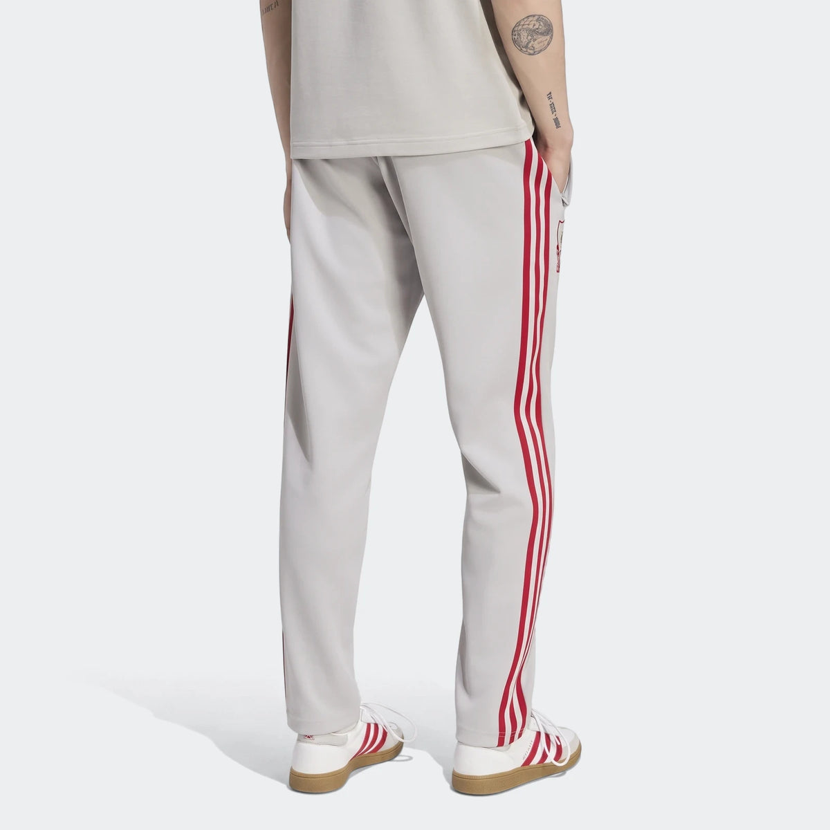 Back view of light grey Adidas Liverpool FC Originals track pants with red stripes, worn by a person with white and red