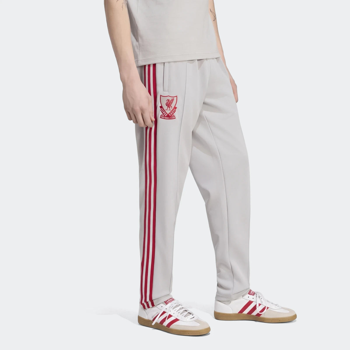 Light grey Liverpool FC Originals track pants with red stripes and club logo, worn by a person, paired with white and red