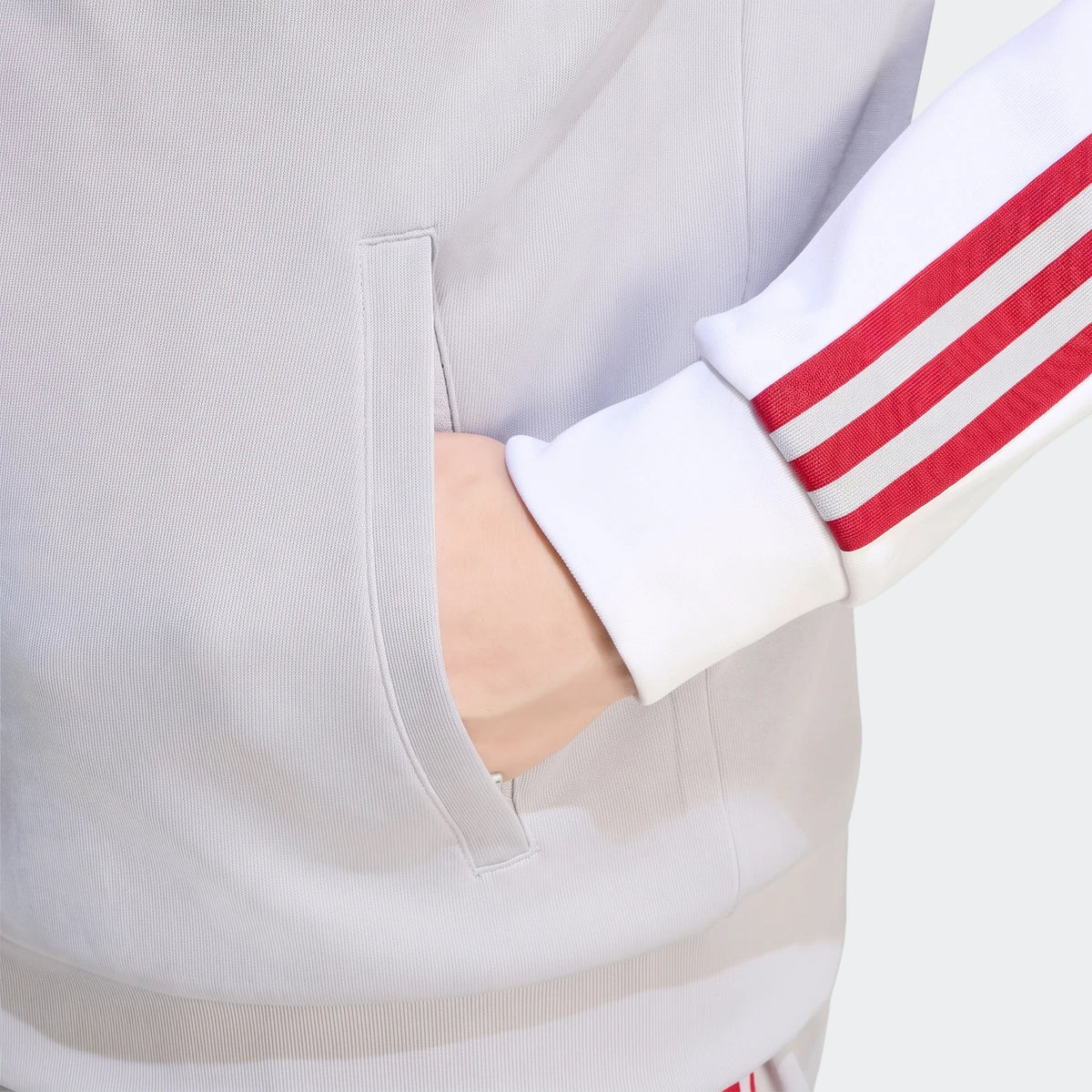 Close-up of a person wearing a light grey Liverpool FC Originals Track Top with a white sleeve and red stripes, hand in